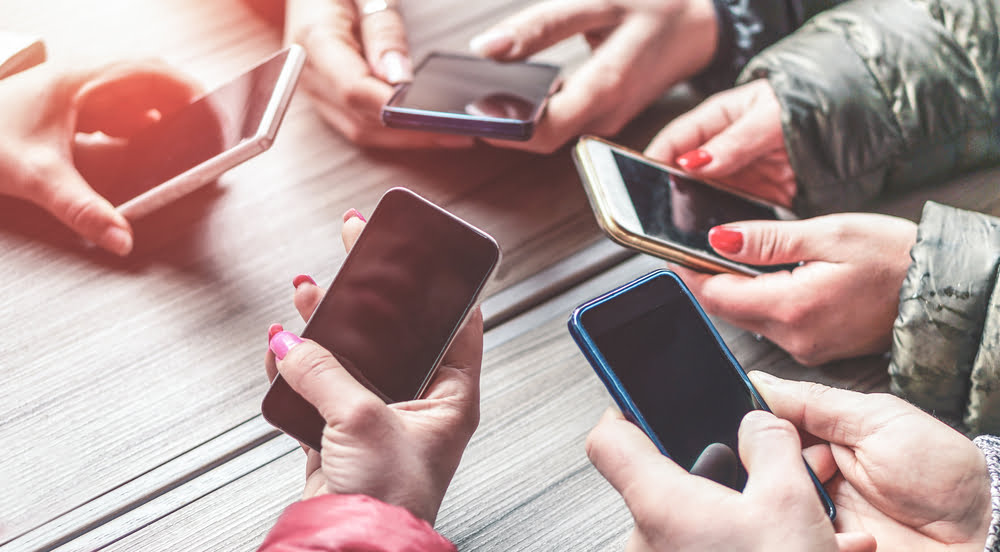 Photo of five people's hands in a circle, all holding their cell phones