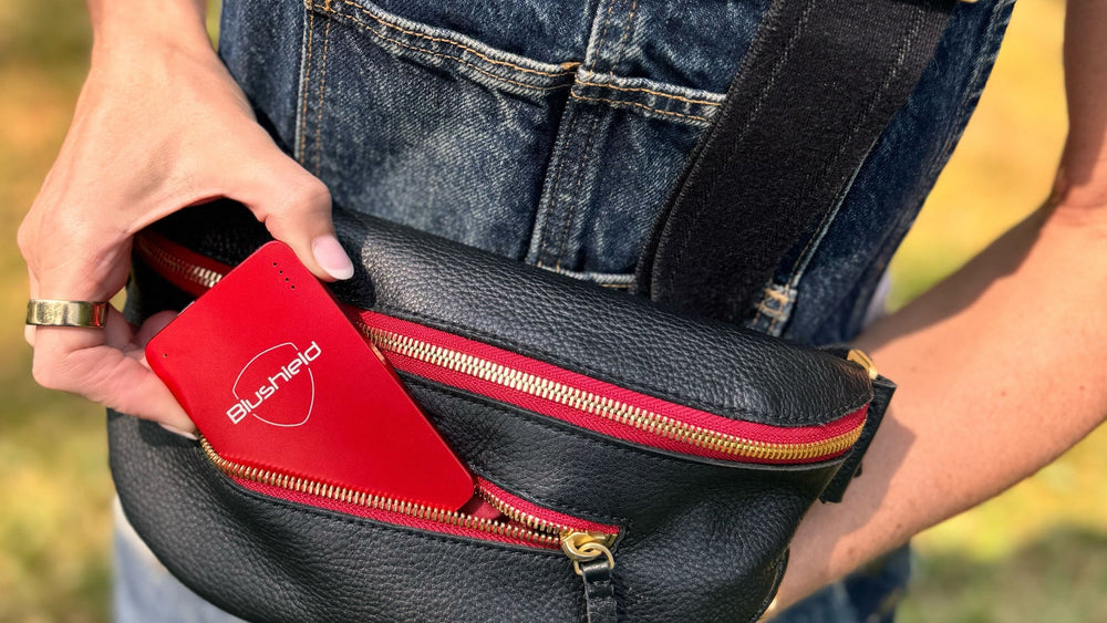 Person holding a black bag with a red portable in pocket, wearing blue overalls.